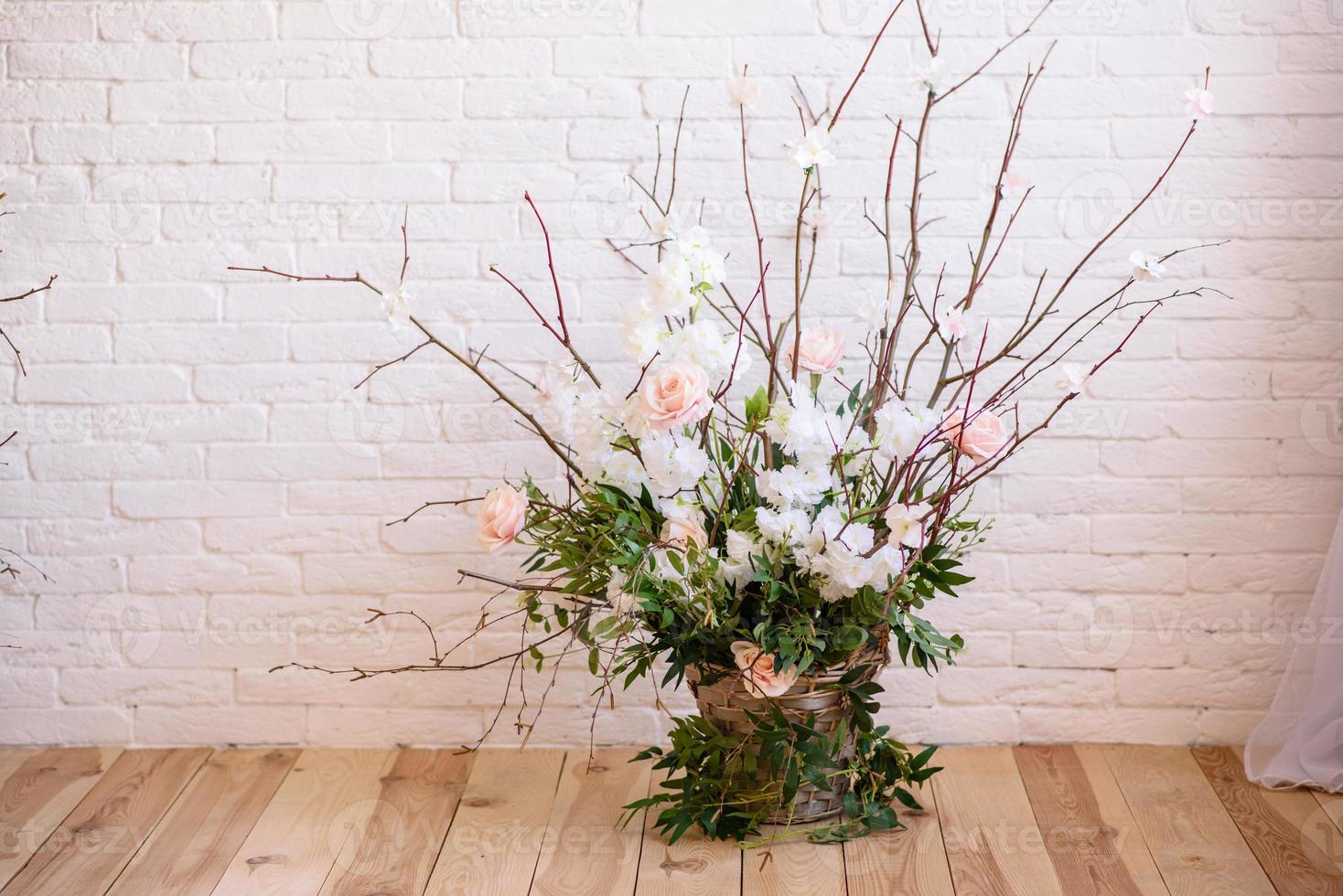 Decoraciones de ramas con hermosas flores rosas y blancas en la canasta con el telón de fondo de una pared de ladrillo blanco. foto