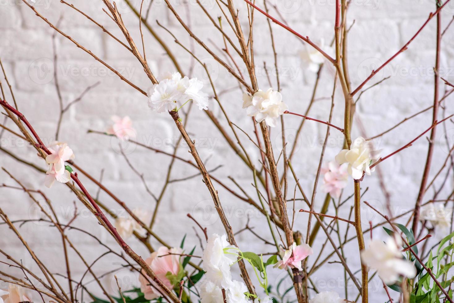 Decoraciones de ramas con hermosas flores rosas y blancas en la canasta con el telón de fondo de una pared de ladrillo blanco. foto