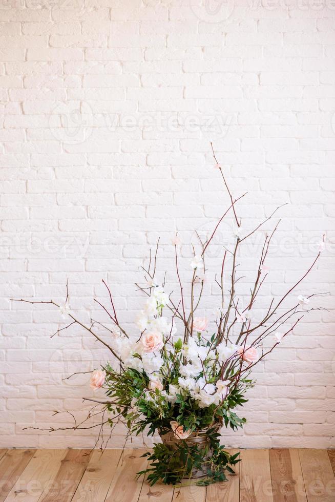 Decorations of branches with beautiful pink and white flowers in the basket against the background of a white brick wall photo