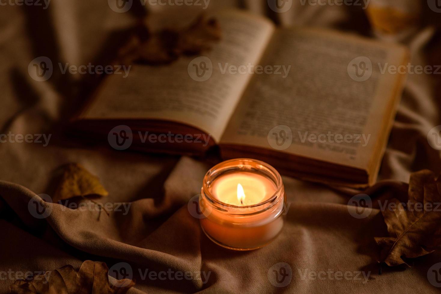 A burning candle on a wooden table in front of a book in a half-mast photo