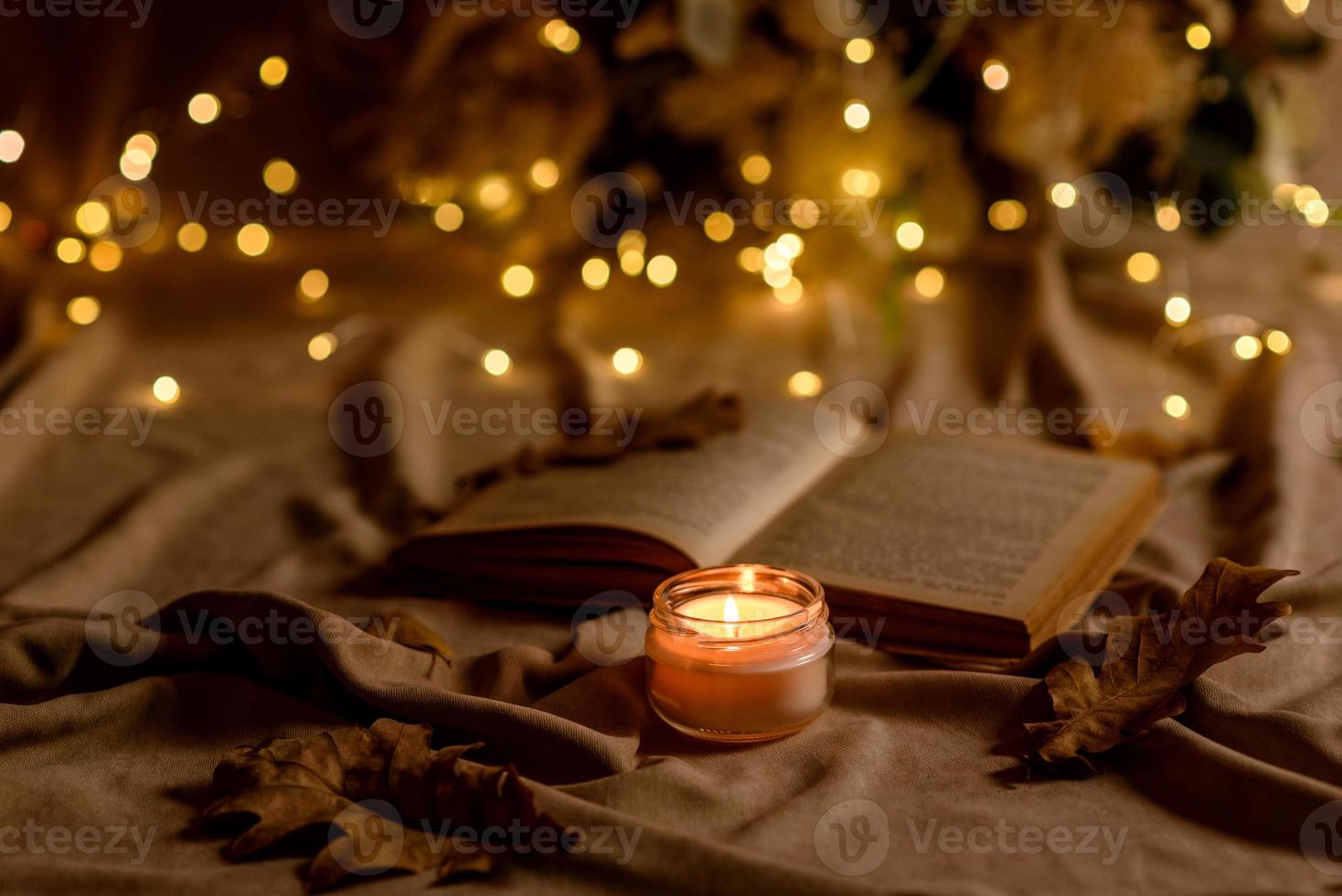 A burning candle on a wooden table in front of a book in a half-mast photo