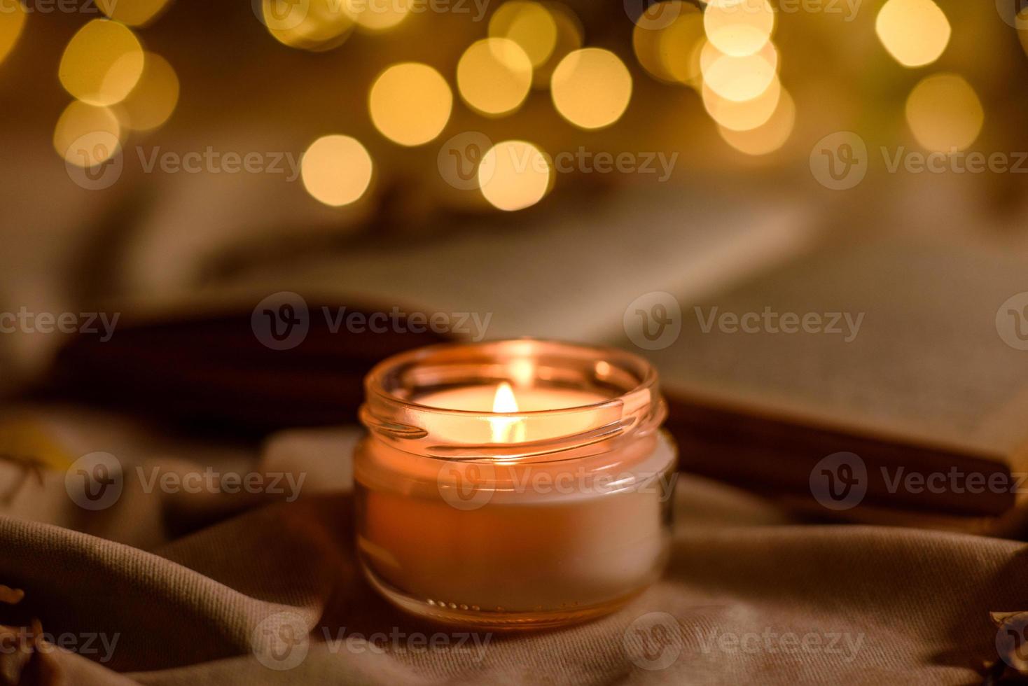 A burning candle on a wooden table in front of a book in a half-mast photo