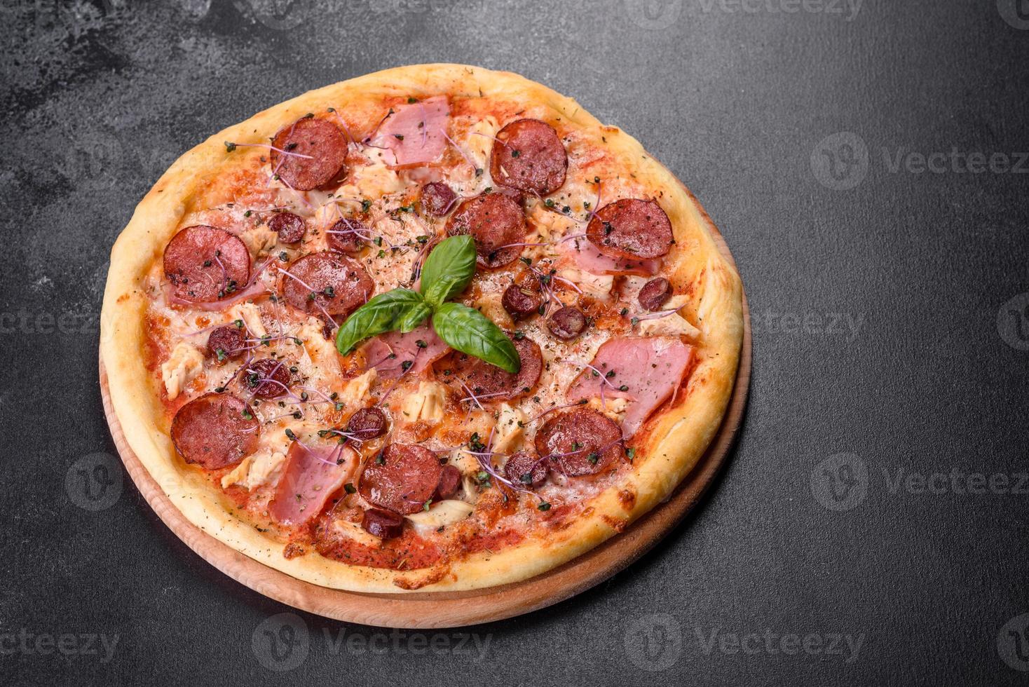 Deliciosa pizza recién horneada con tomates, salami y tocino sobre un fondo de hormigón oscuro foto