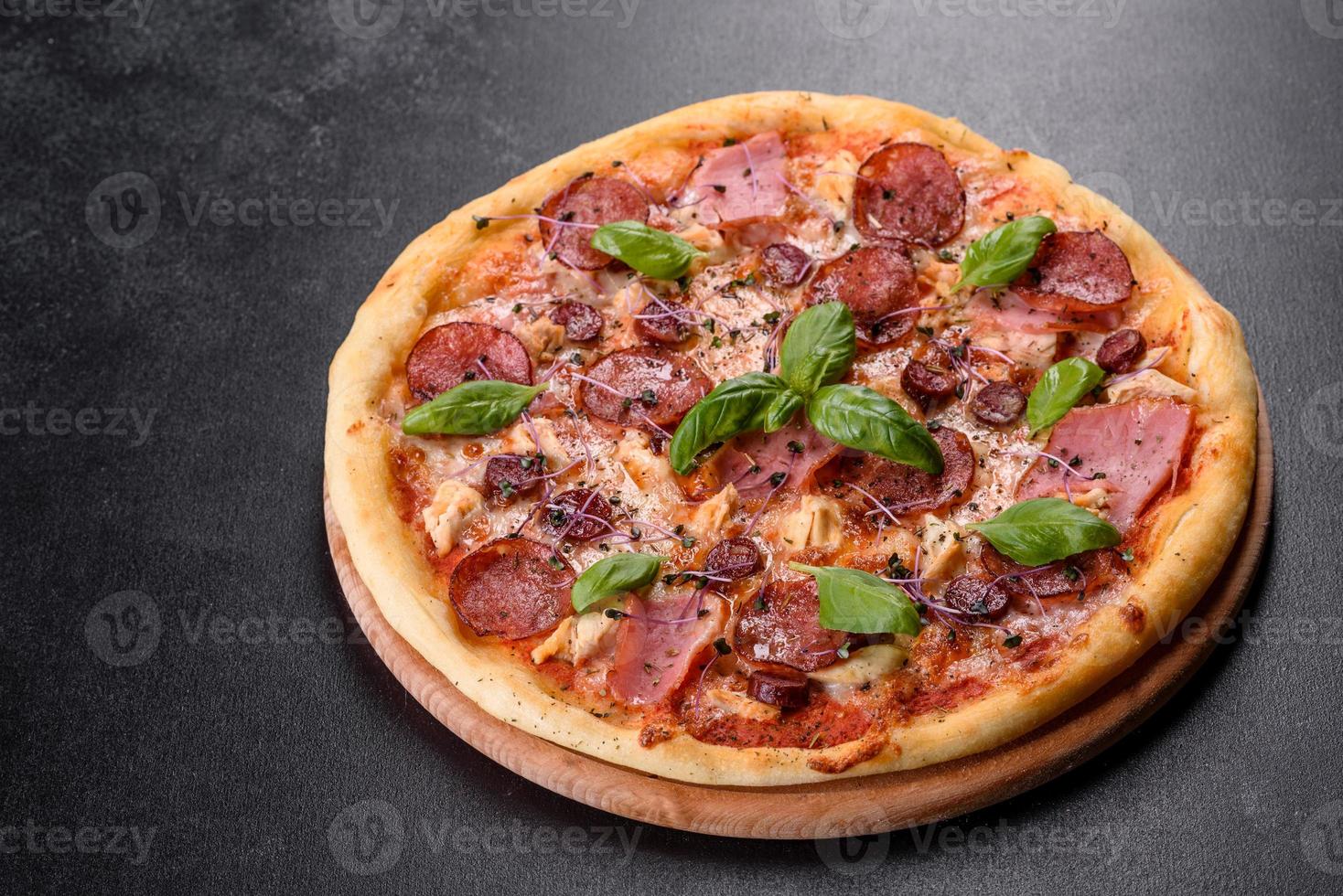 Deliciosa pizza recién horneada con tomates, salami y tocino sobre un fondo de hormigón oscuro foto