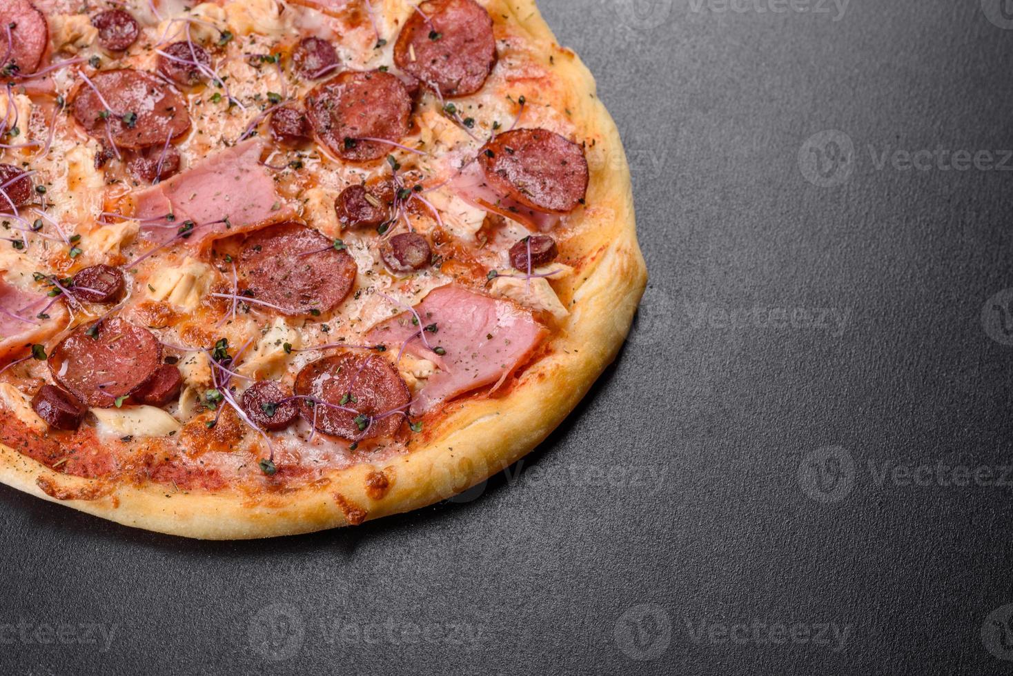 Deliciosa pizza recién horneada con tomates, salami y tocino sobre un fondo de hormigón oscuro foto