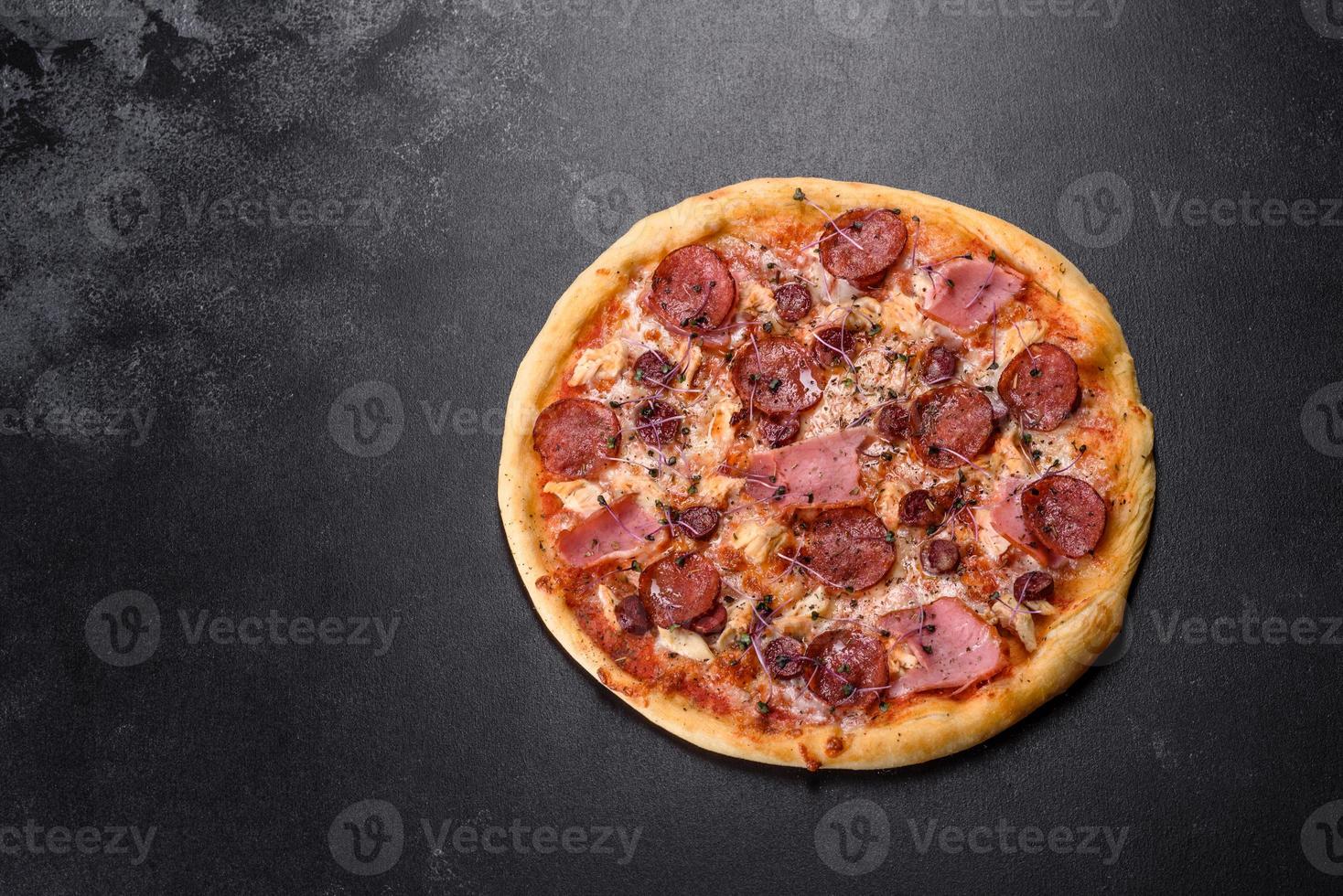 Delicious fresh oven pizza with tomatoes, salami and bacon on a dark concrete background photo