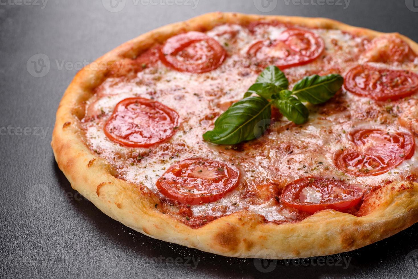 Sabrosa pizza recién horneada con tomate, queso y albahaca sobre un fondo de hormigón foto