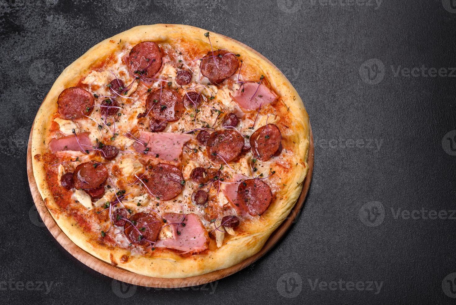 Deliciosa pizza recién horneada con tomates, salami y tocino sobre un fondo de hormigón oscuro foto