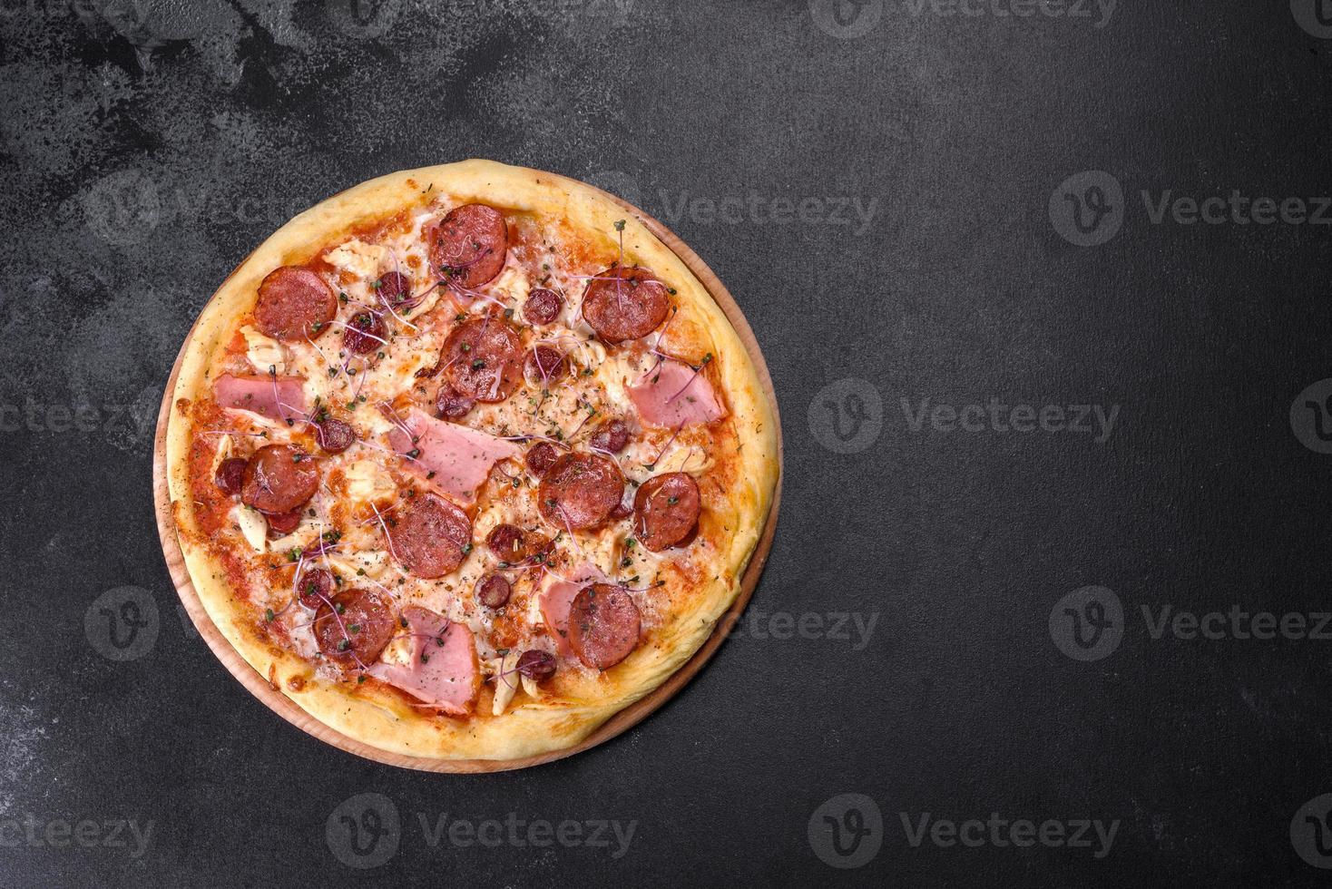 Deliciosa pizza recién horneada con tomates, salami y tocino sobre un fondo de hormigón oscuro foto