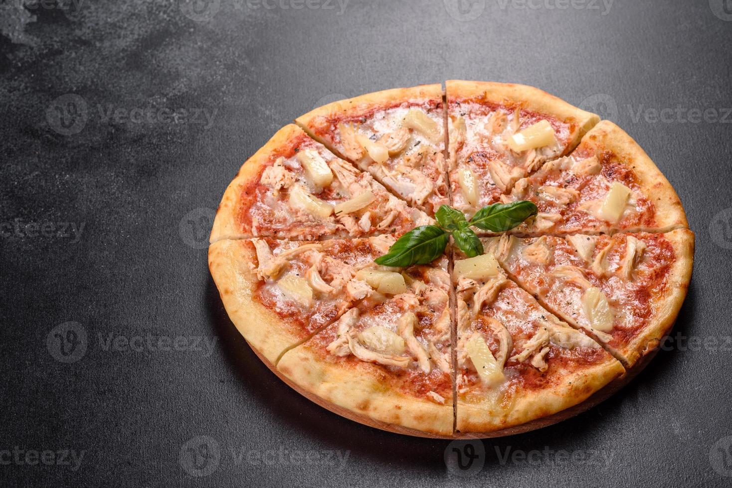 Sabrosa pizza recién horneada con tomate, queso y piña sobre un fondo de hormigón oscuro foto