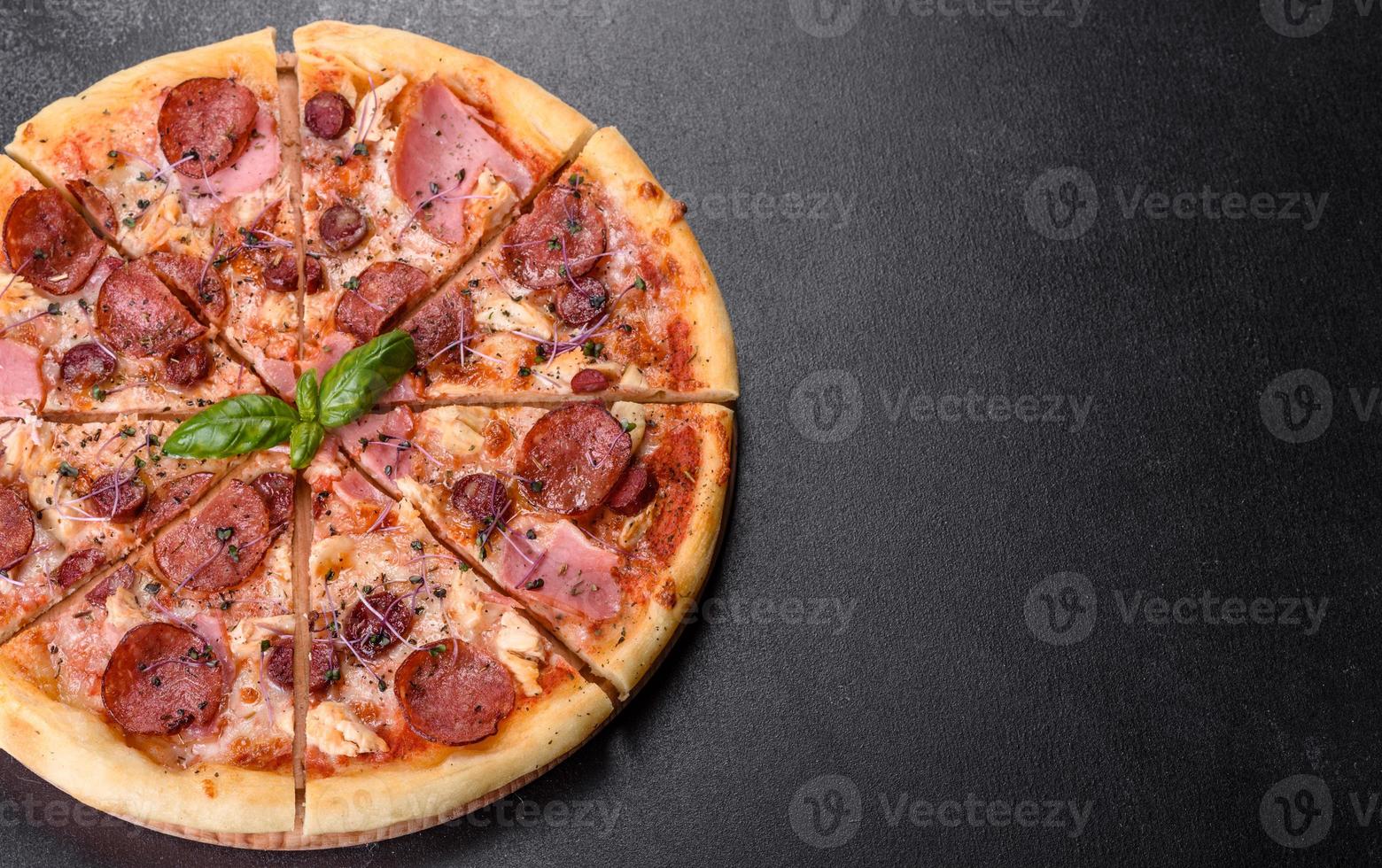 Delicious fresh oven pizza with tomatoes, salami and bacon on a dark concrete background photo