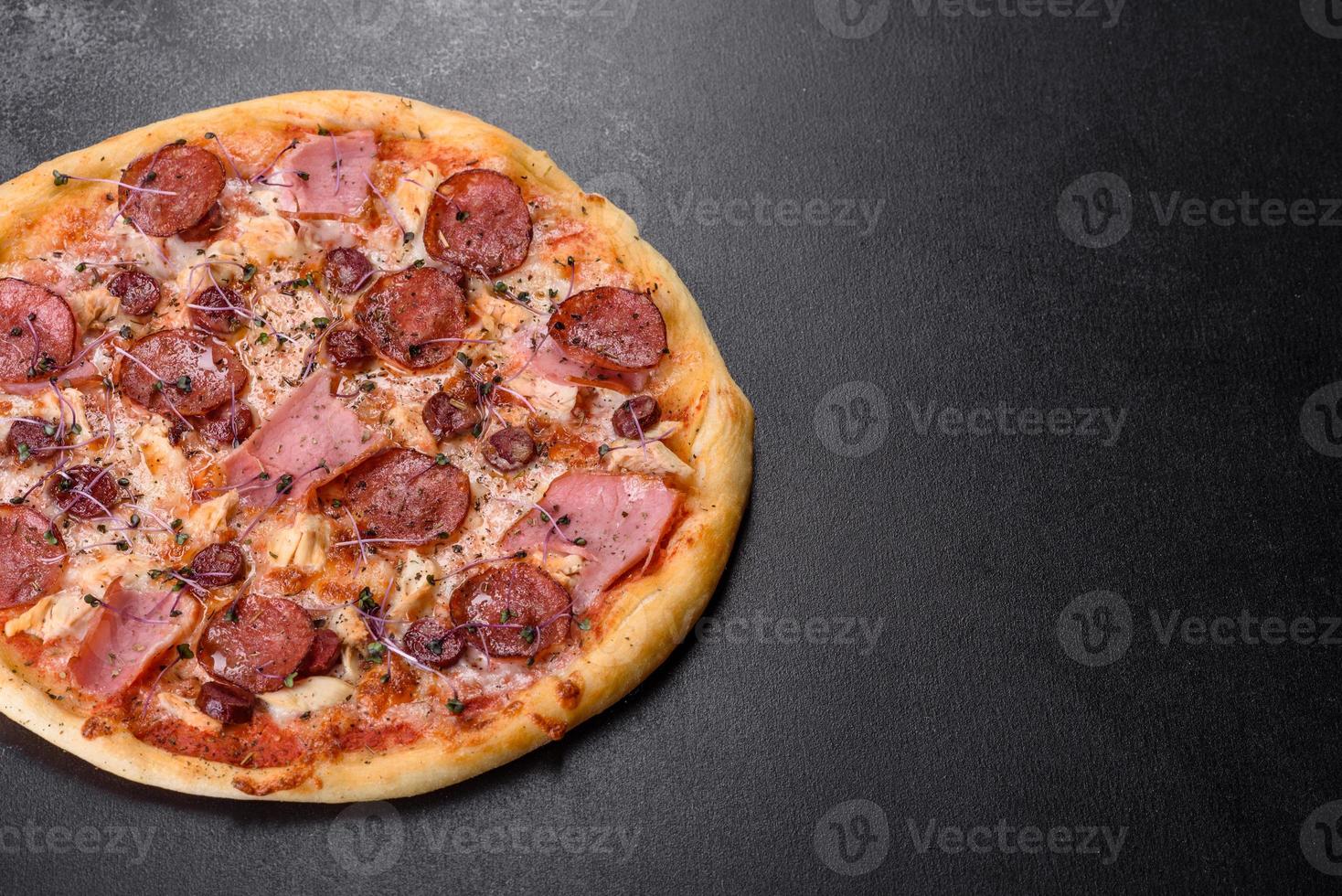 Deliciosa pizza recién horneada con tomates, salami y tocino sobre un fondo de hormigón oscuro foto