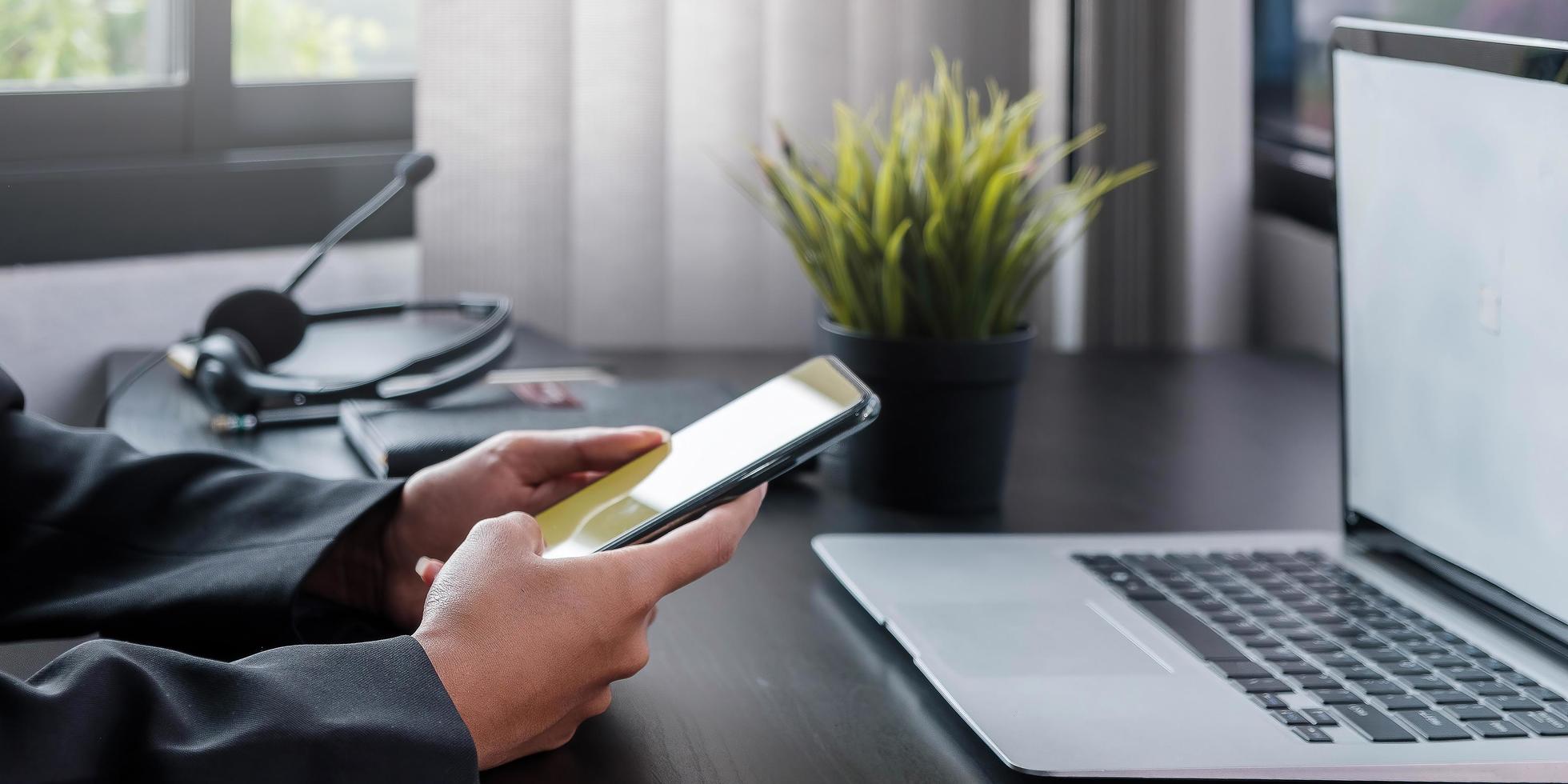 Shot of business woman holding smartphone getting message during making transaction on laptop computer photo