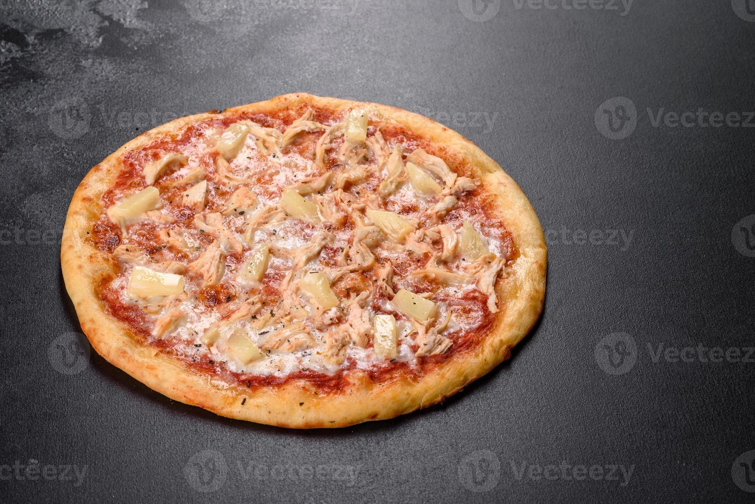 Sabrosa pizza recién horneada con tomate, queso y piña sobre un fondo de hormigón oscuro foto