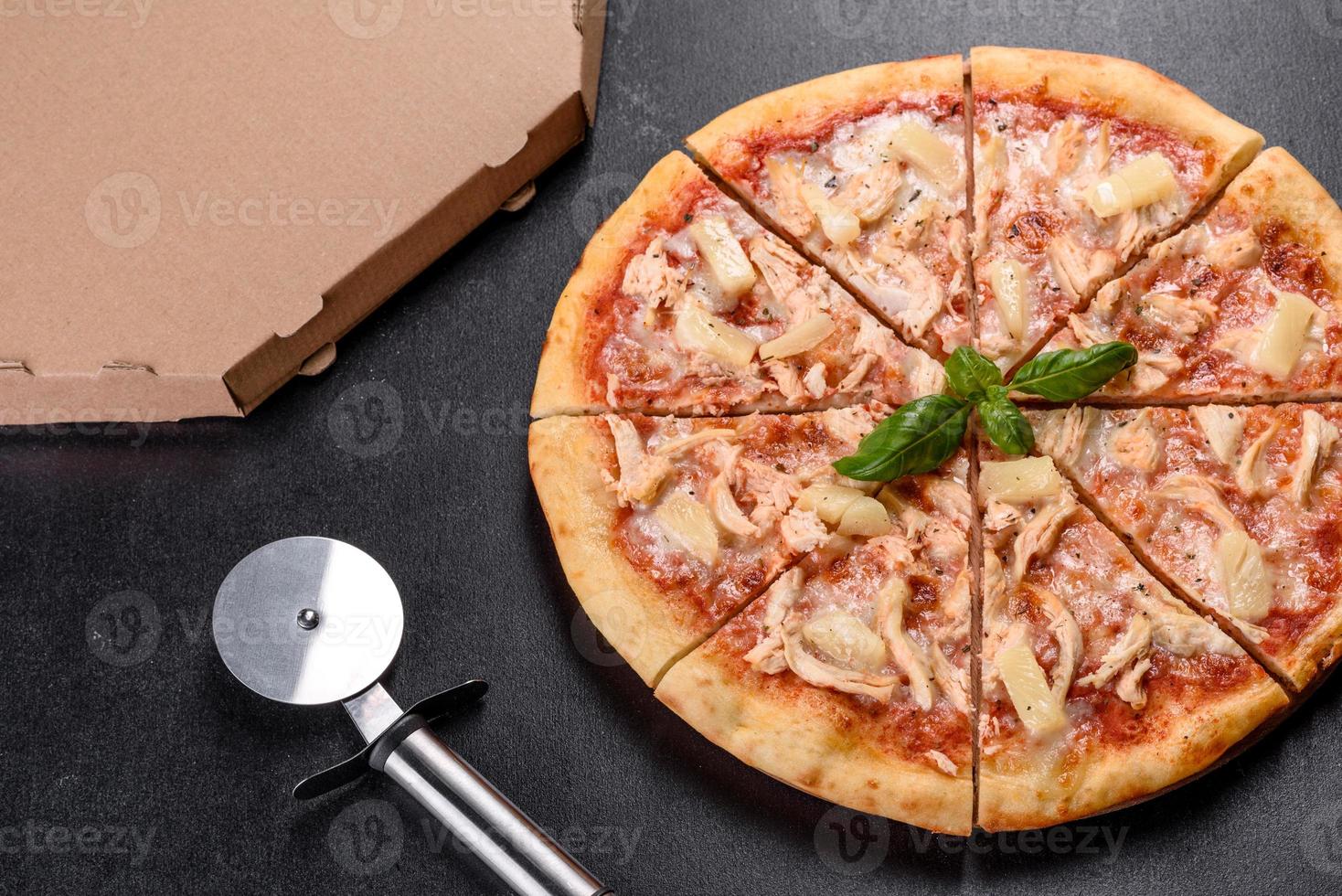 Sabrosa pizza recién horneada con tomate, queso y piña sobre un fondo de hormigón oscuro foto