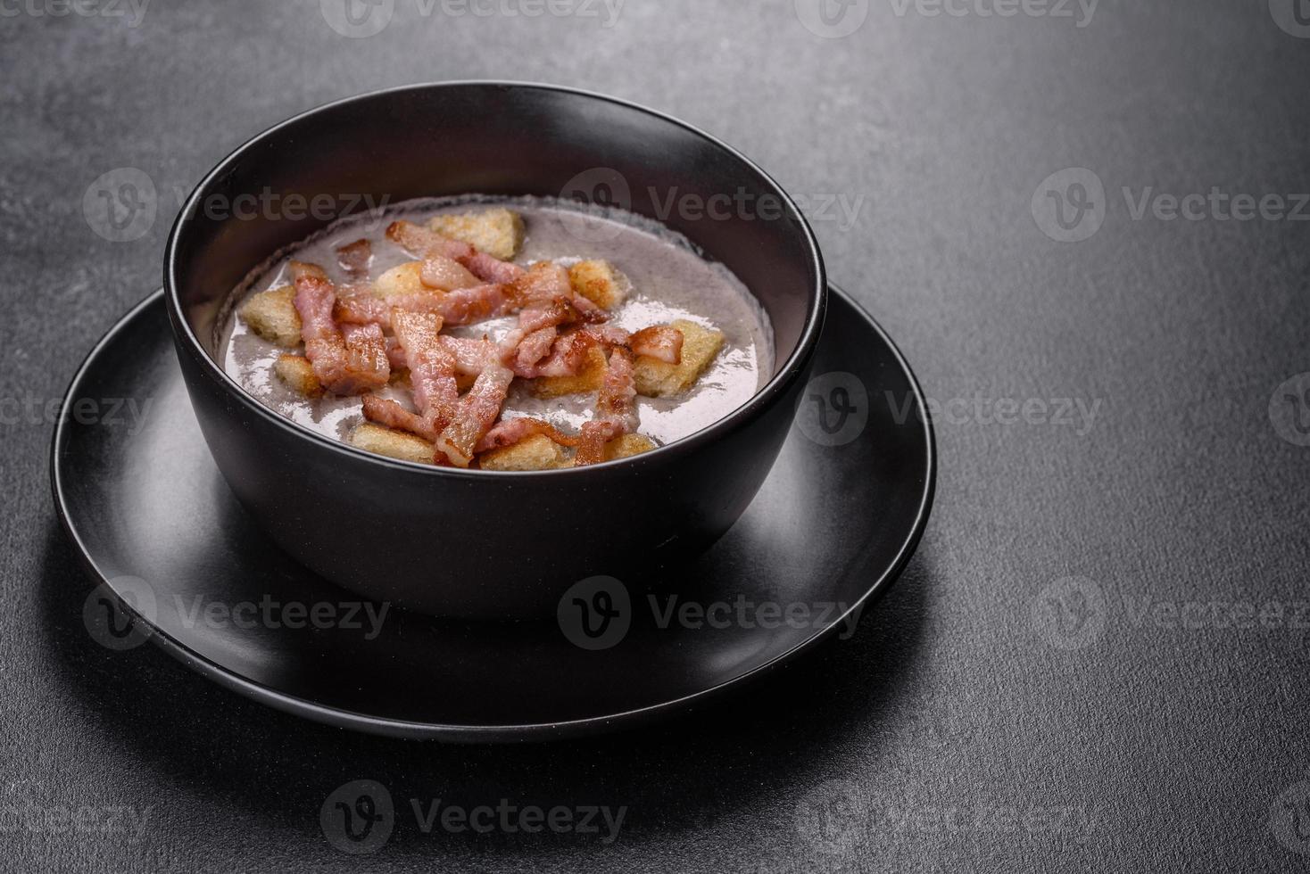 Fresh delicious hot puree soup with mushrooms and bacon in a black plate photo