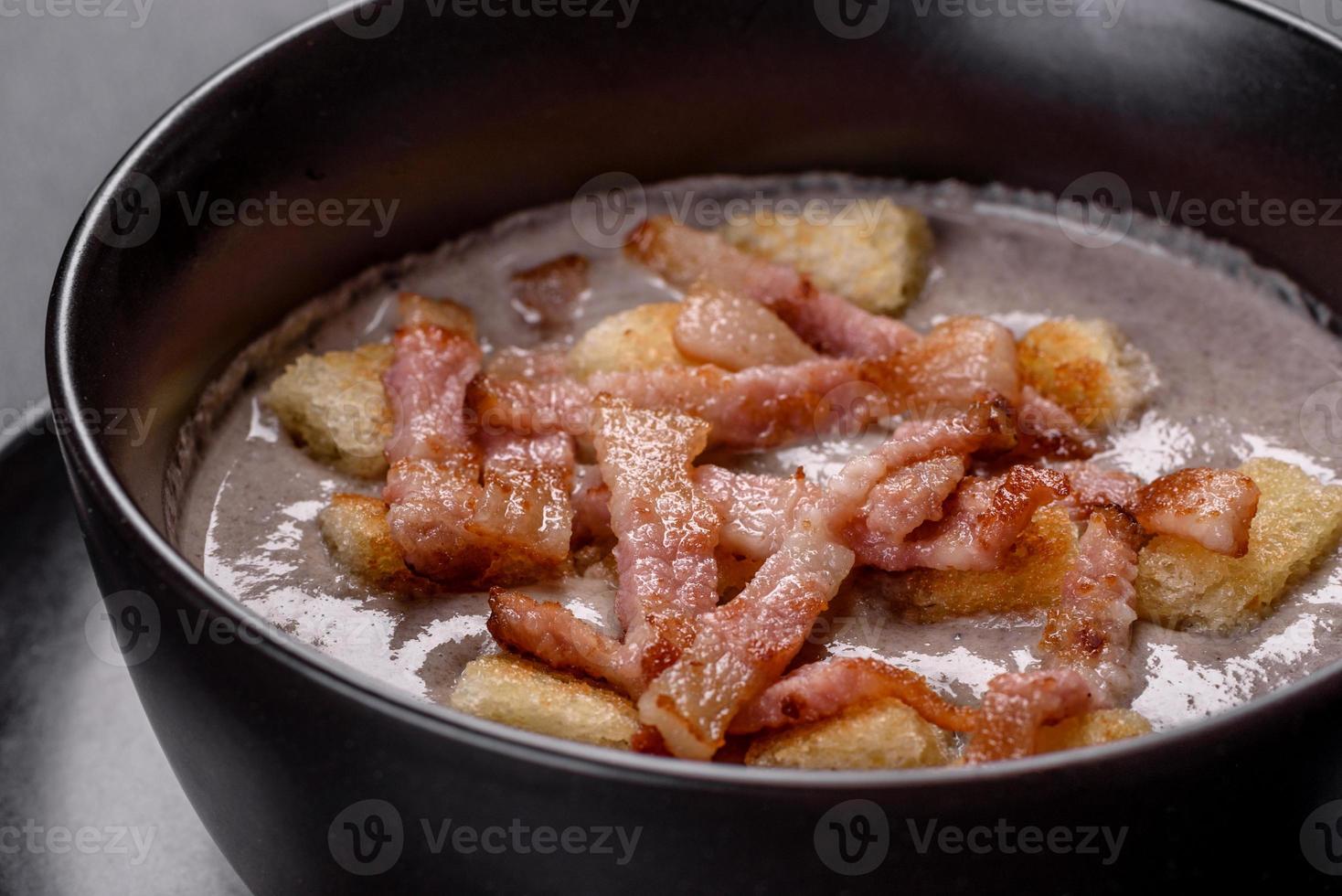 Fresh delicious hot puree soup with mushrooms and bacon in a black plate photo