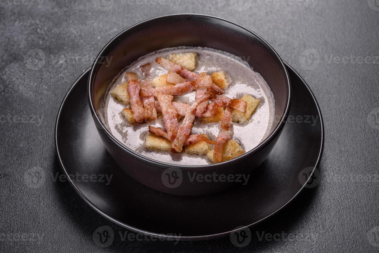 Fresh delicious hot puree soup with mushrooms and bacon in a black plate photo