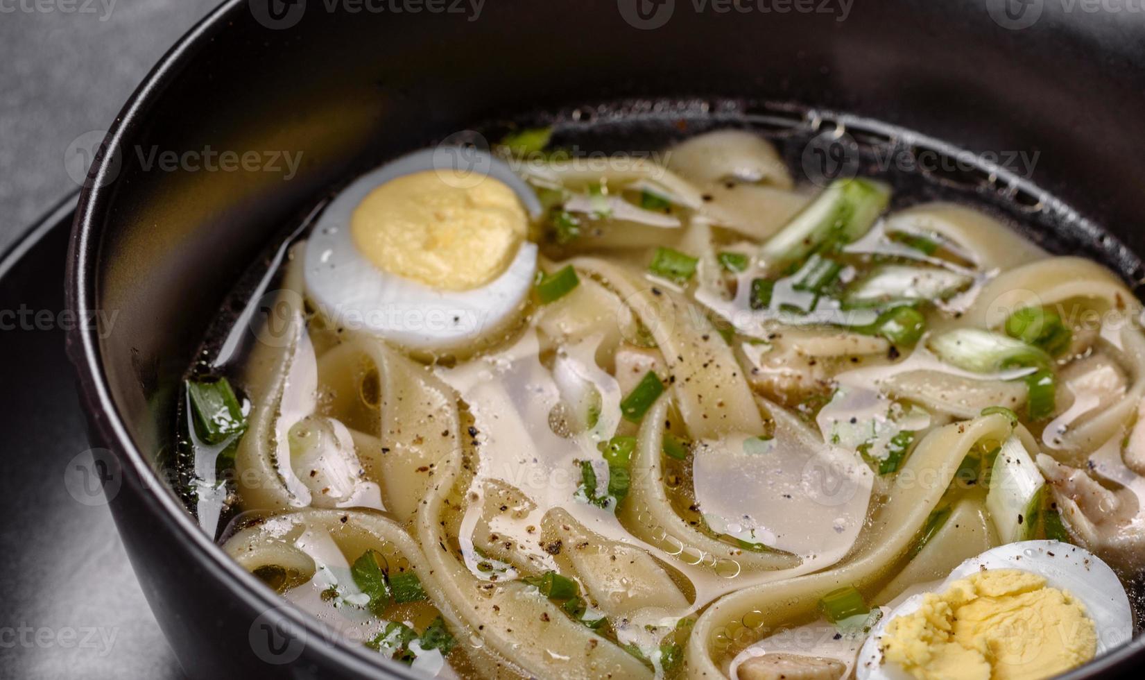 Deliciosa sopa caliente fresca con fideos y huevo de codorniz en una placa negra foto