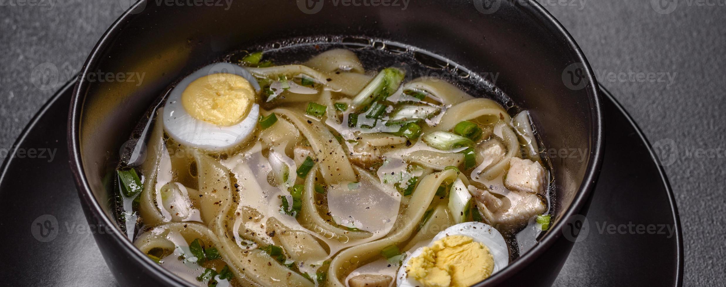 Deliciosa sopa caliente fresca con fideos y huevo de codorniz en una placa negra foto