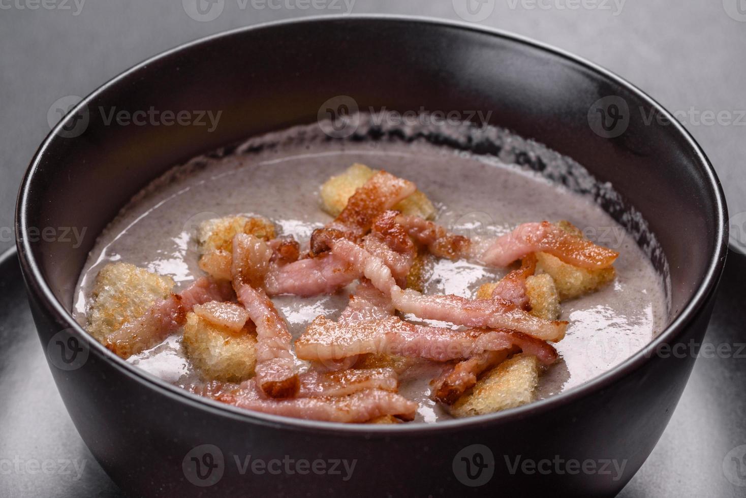 Fresh delicious hot puree soup with mushrooms and bacon in a black plate photo