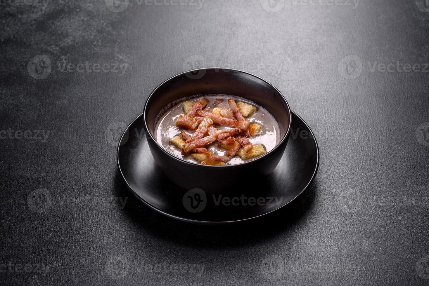 Fresh delicious hot puree soup with mushrooms and bacon in a black plate photo