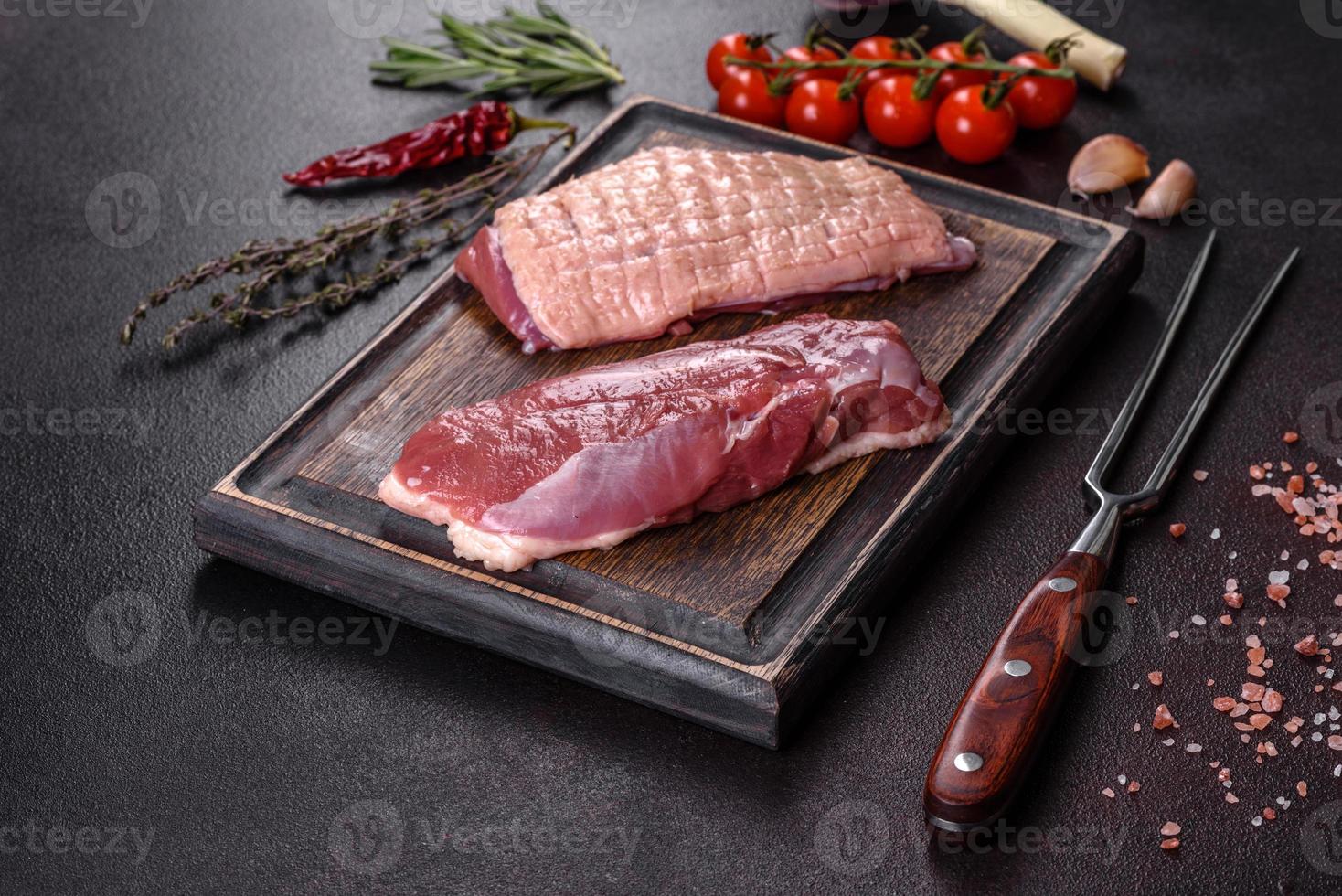 Raw duck breast with herbs and spices on a dark concrete background photo