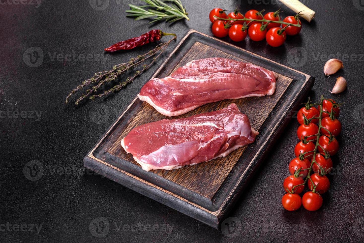 Raw duck breast with herbs and spices on a dark concrete background photo