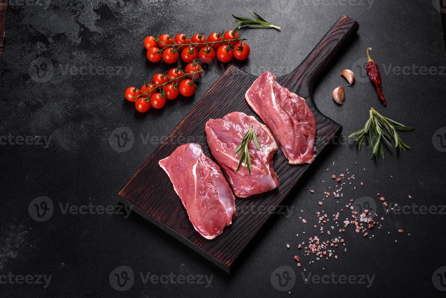 Raw duck breast with herbs and spices on a dark concrete background photo