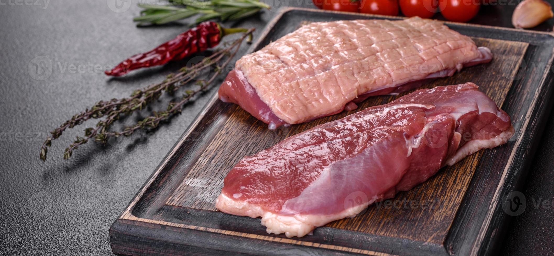 Raw duck breast with herbs and spices on a dark concrete background photo