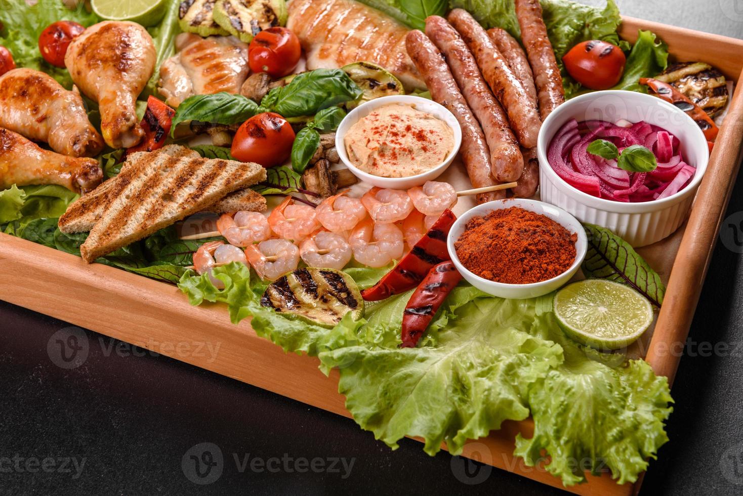 Composition of sausages, chicken, pork and shrimp prepared on grill, as well as vegetables prepared on grill with spices and herbs photo