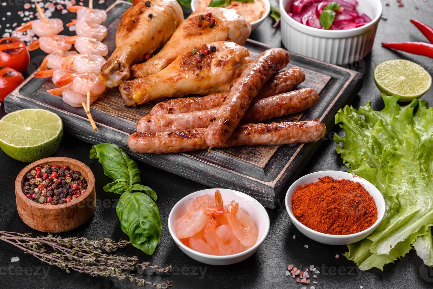 Composition of sausages, chicken, pork and shrimp prepared on grill, as well as vegetables prepared on grill with spices and herbs photo