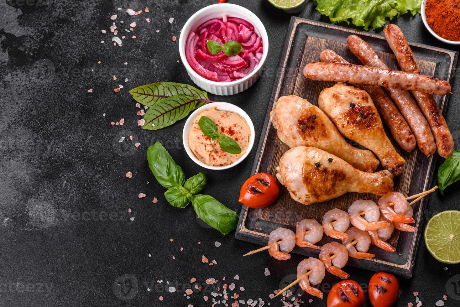 Composition of sausages, chicken, pork and shrimp prepared on grill, as well as vegetables prepared on grill with spices and herbs photo