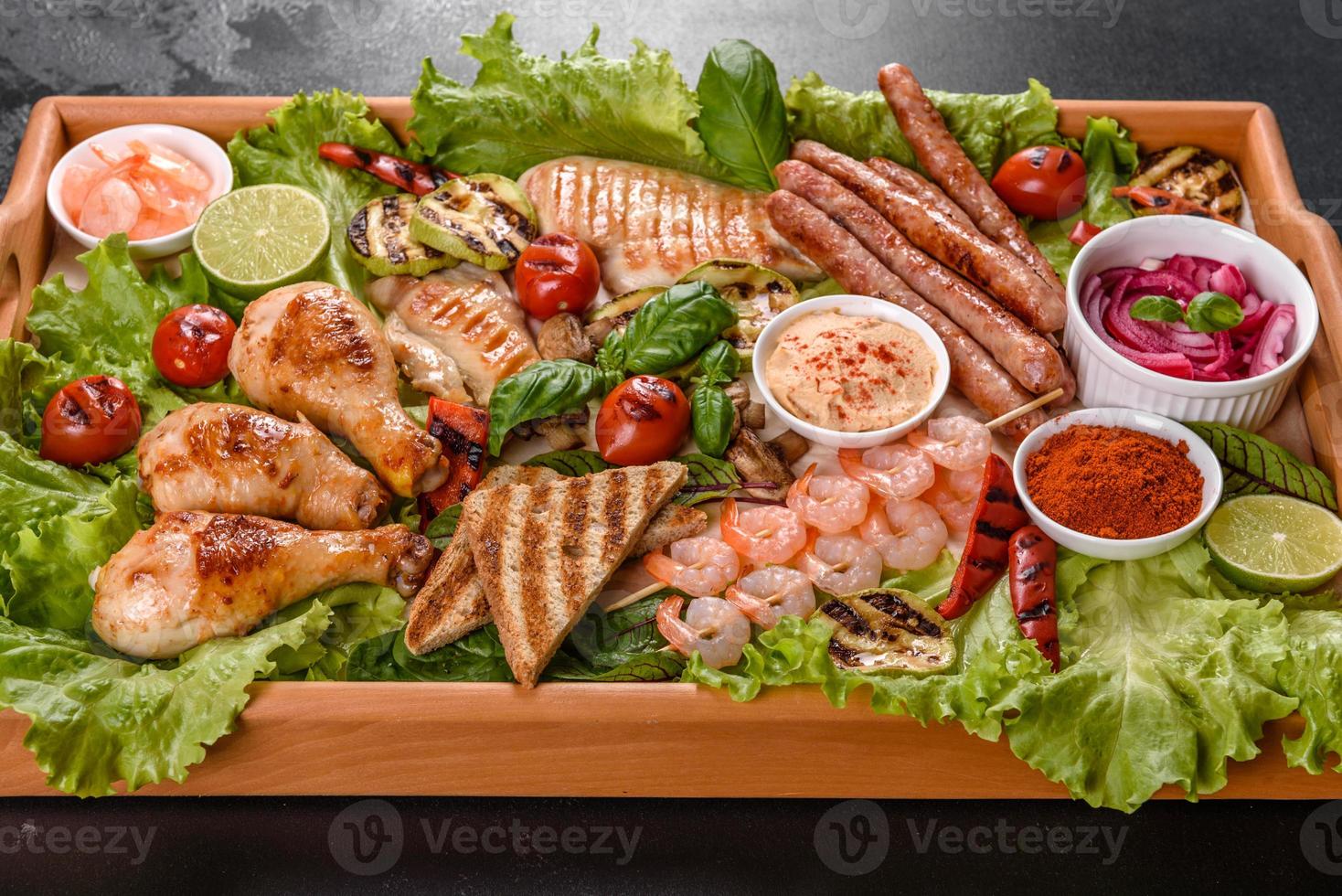 Composition of sausages, chicken, pork and shrimp prepared on grill, as well as vegetables prepared on grill with spices and herbs photo