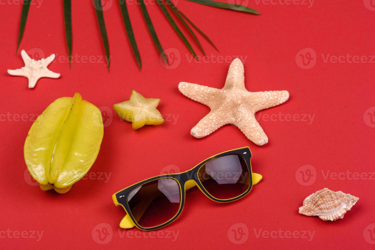 Carambol de frutas, accesorios de playa y follaje de una planta tropical sobre papel de colores foto