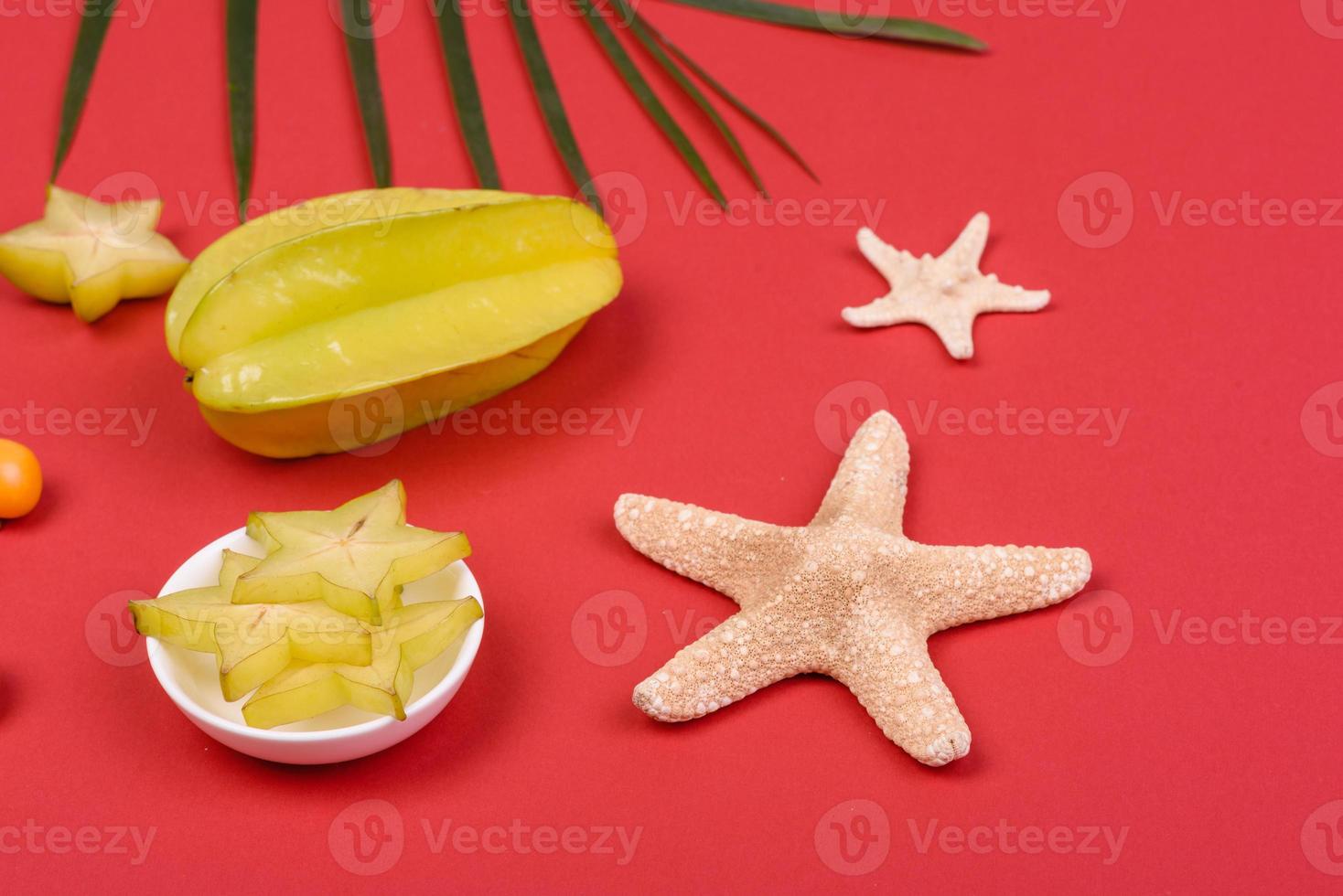 Carambol de frutas, accesorios de playa y follaje de una planta tropical sobre papel de colores foto