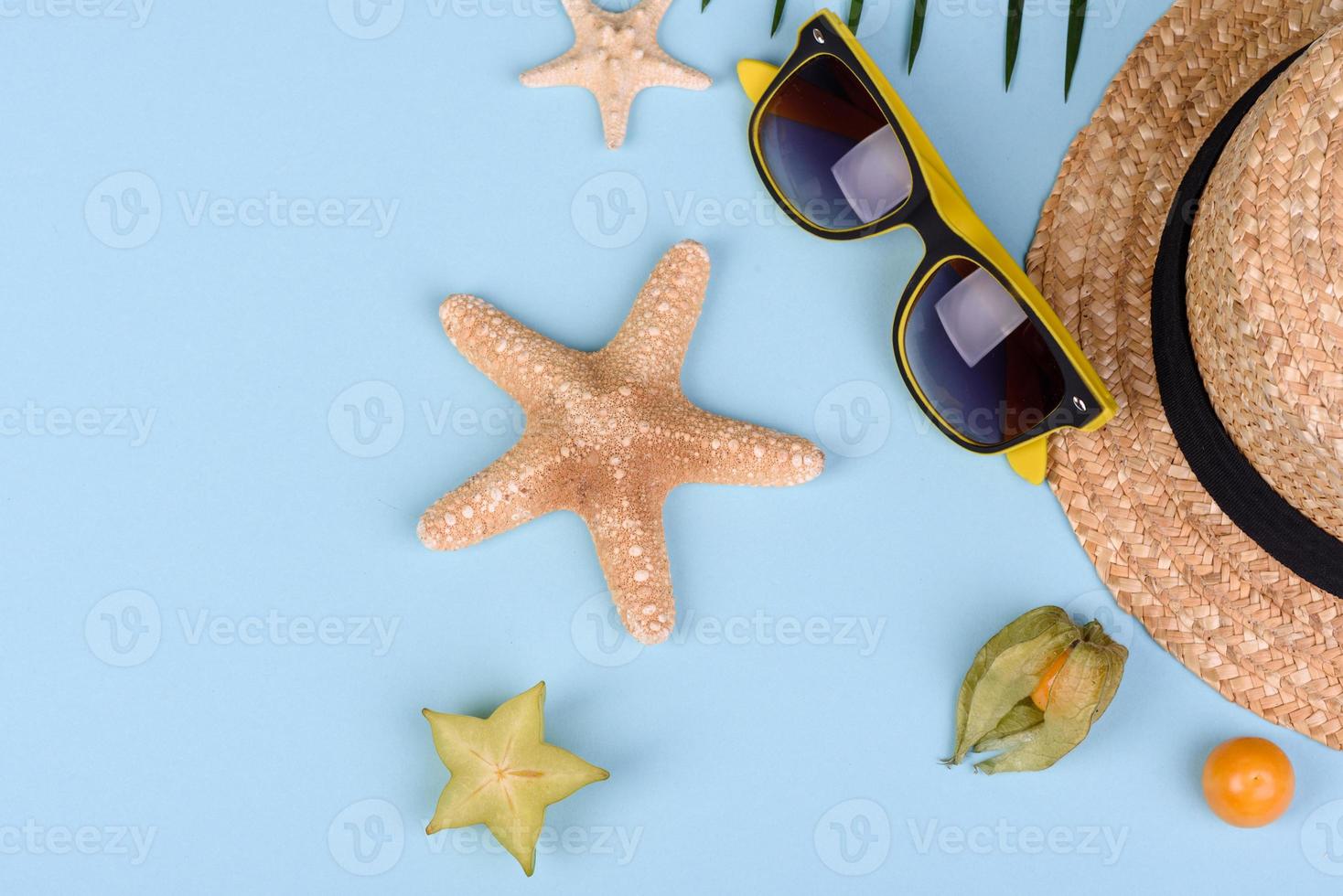 Carambol de frutas, accesorios de playa y follaje de una planta tropical sobre papel de colores foto