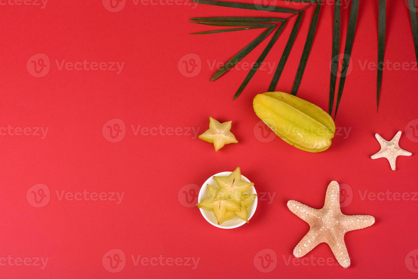 Fruit carambol, beach accessories and foliage of a tropical plant on colored paper photo