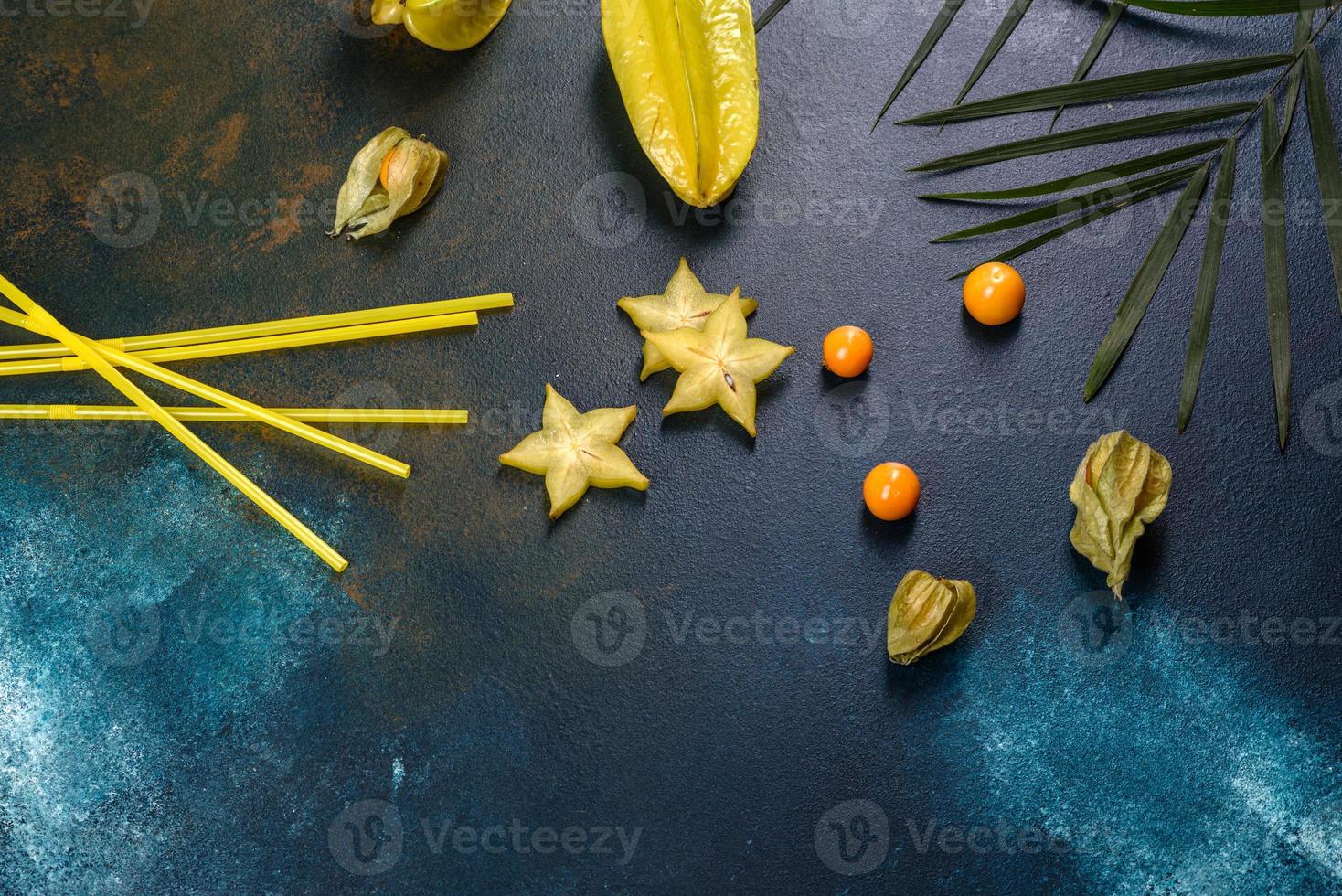 Carambol de frutas, accesorios de playa y follaje de una planta tropical sobre papel de colores foto