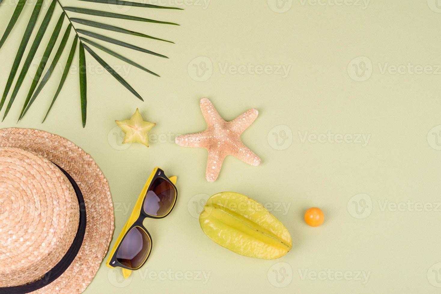 Carambol de frutas, accesorios de playa y follaje de una planta tropical sobre papel de colores foto