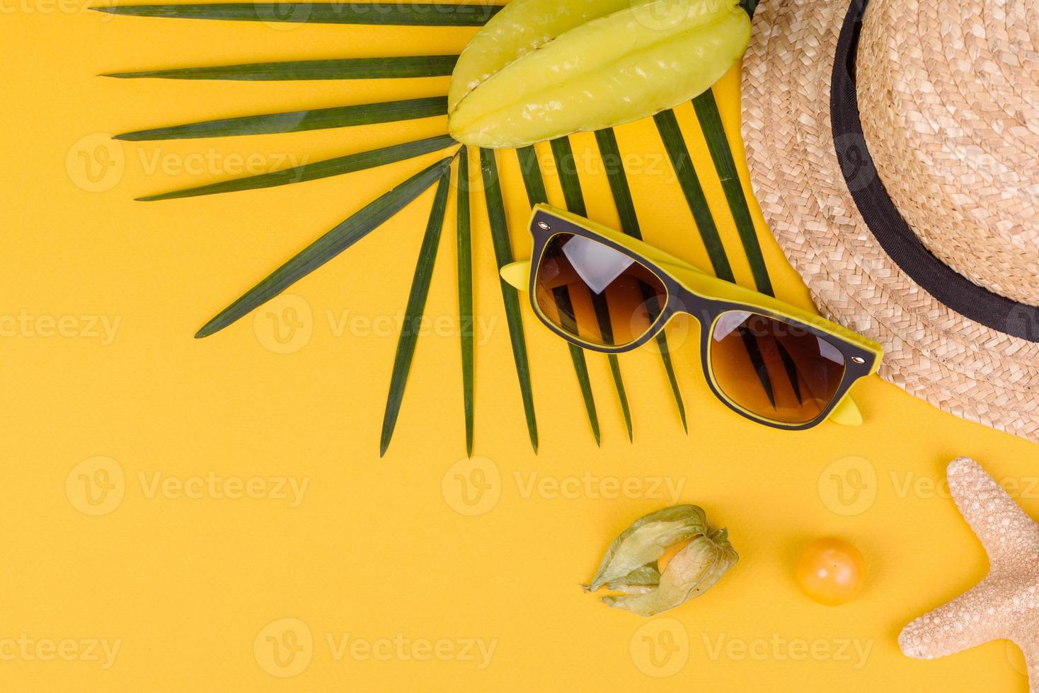 Fruit carambol, beach accessories and foliage of a tropical plant on colored paper photo