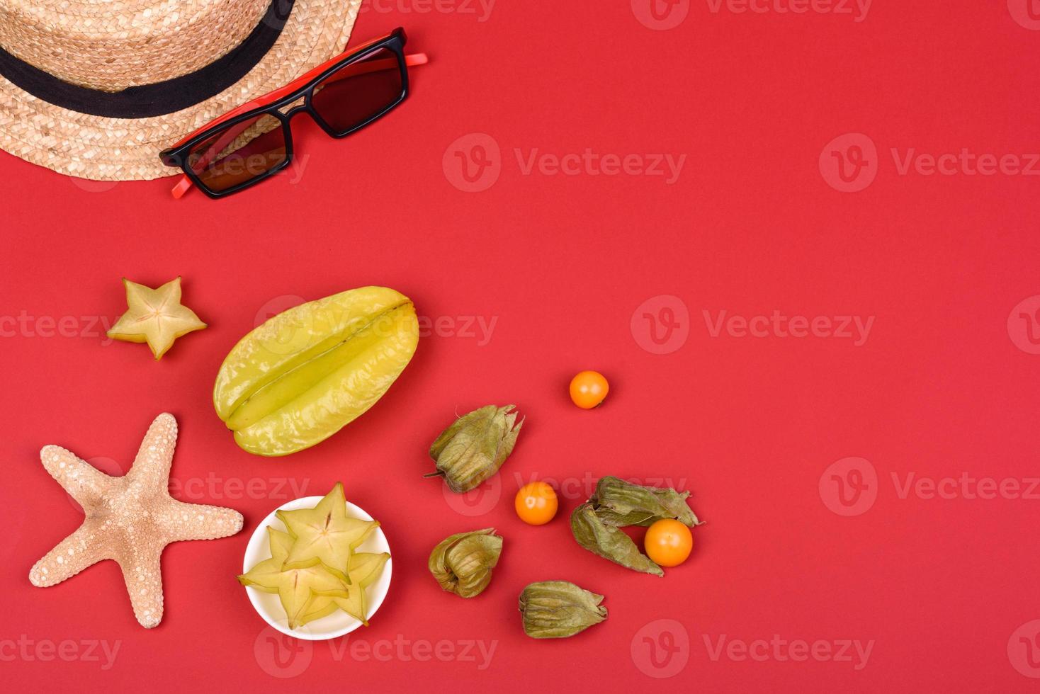 Carambol de frutas, accesorios de playa y follaje de una planta tropical sobre papel de colores foto