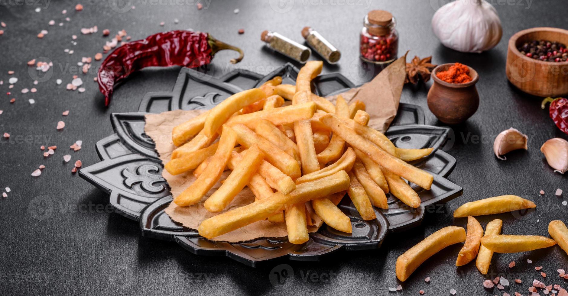 Tasty fried french fries with salt and spices on a dark background photo