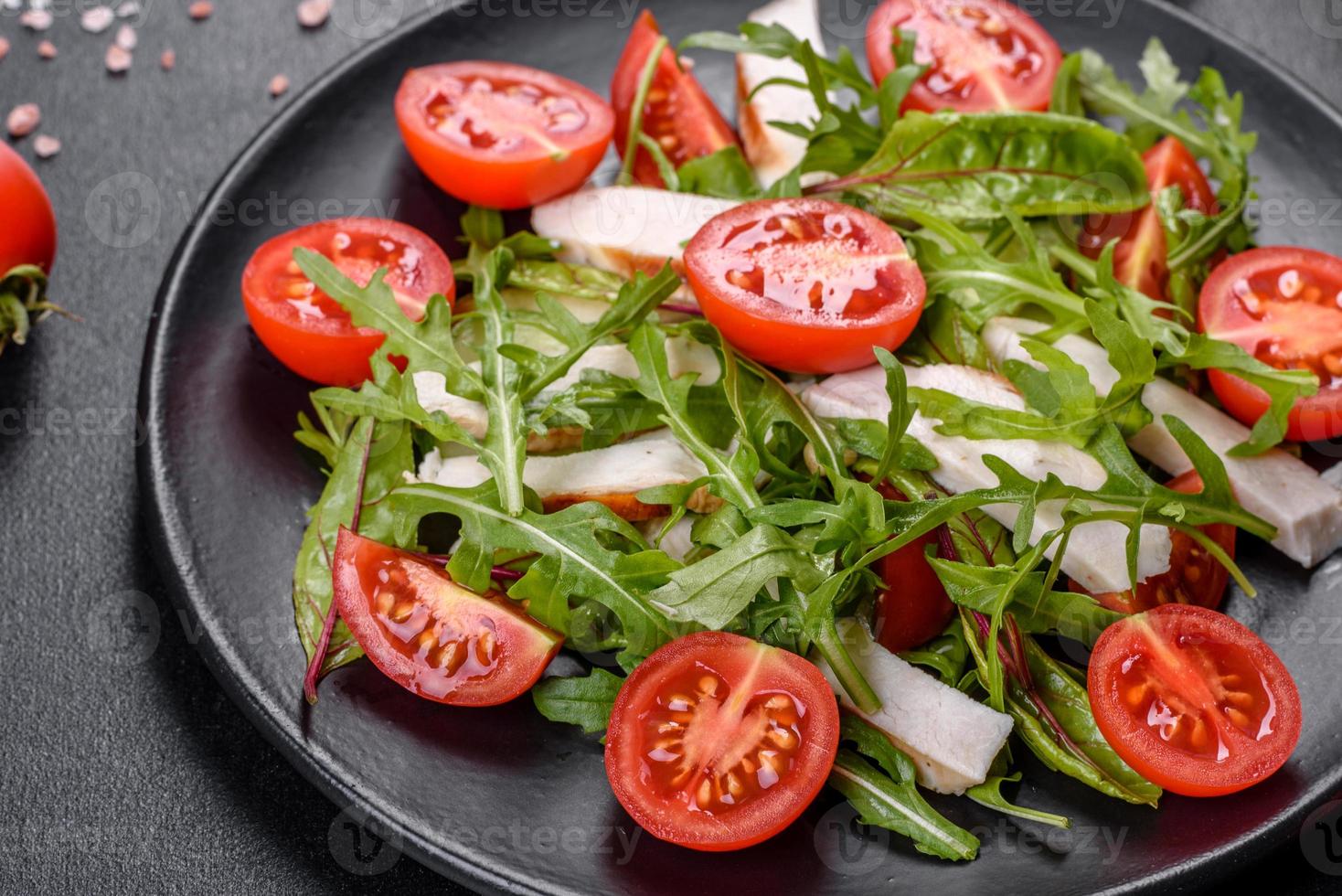 Pieces of chicken, tomatoes and lettuce leaves on a dark concrete background photo