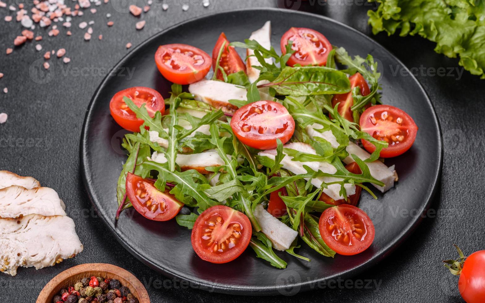 Trozos de pollo, tomates y hojas de lechuga sobre un fondo de hormigón oscuro foto