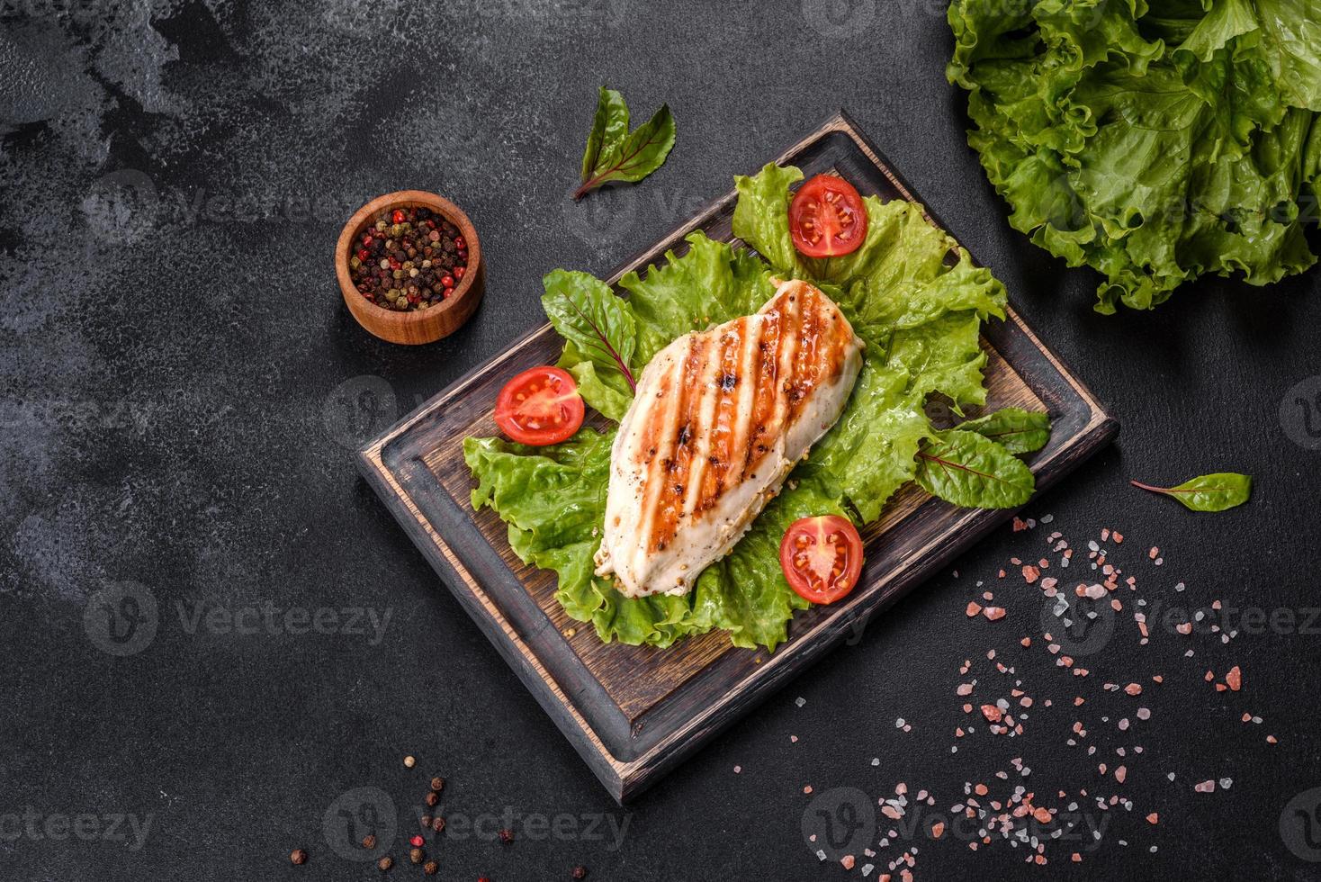 Trozos de pollo, tomates y hojas de lechuga sobre un fondo de hormigón oscuro foto