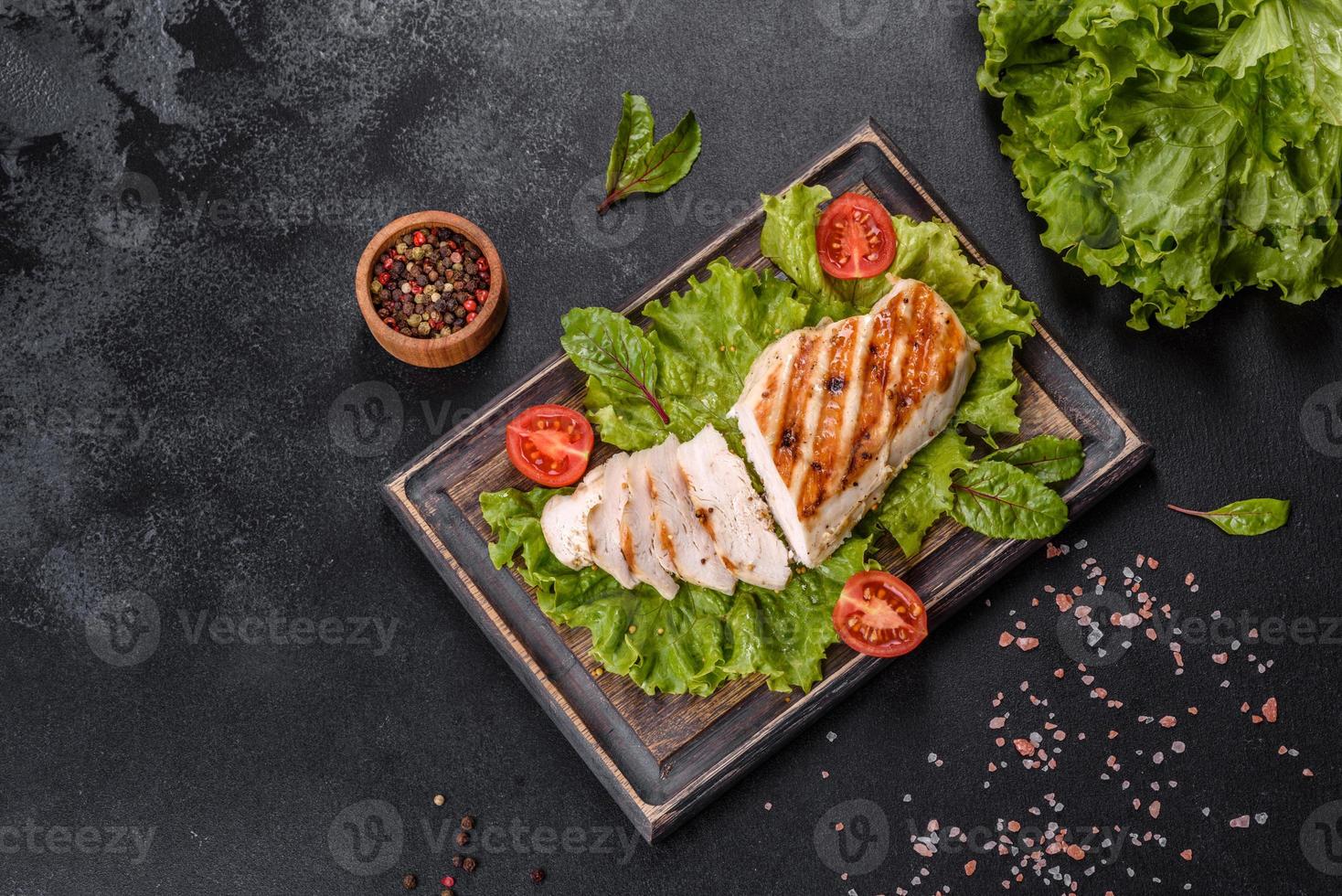 Trozos de pollo, tomates y hojas de lechuga sobre un fondo de hormigón oscuro foto