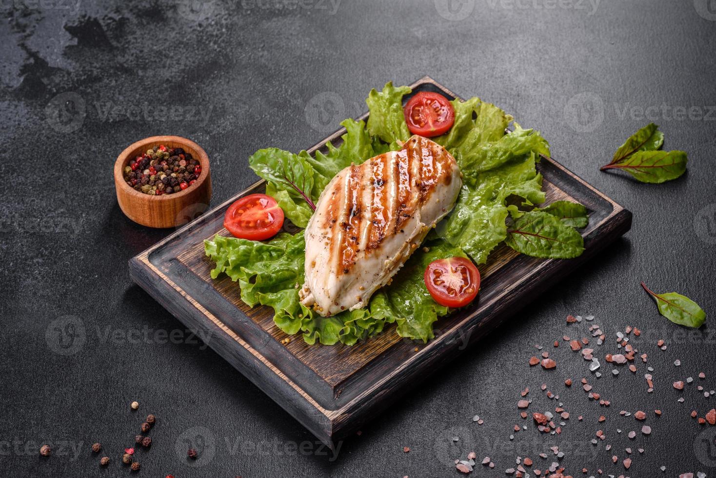 Pieces of chicken, tomatoes and lettuce leaves on a dark concrete background photo