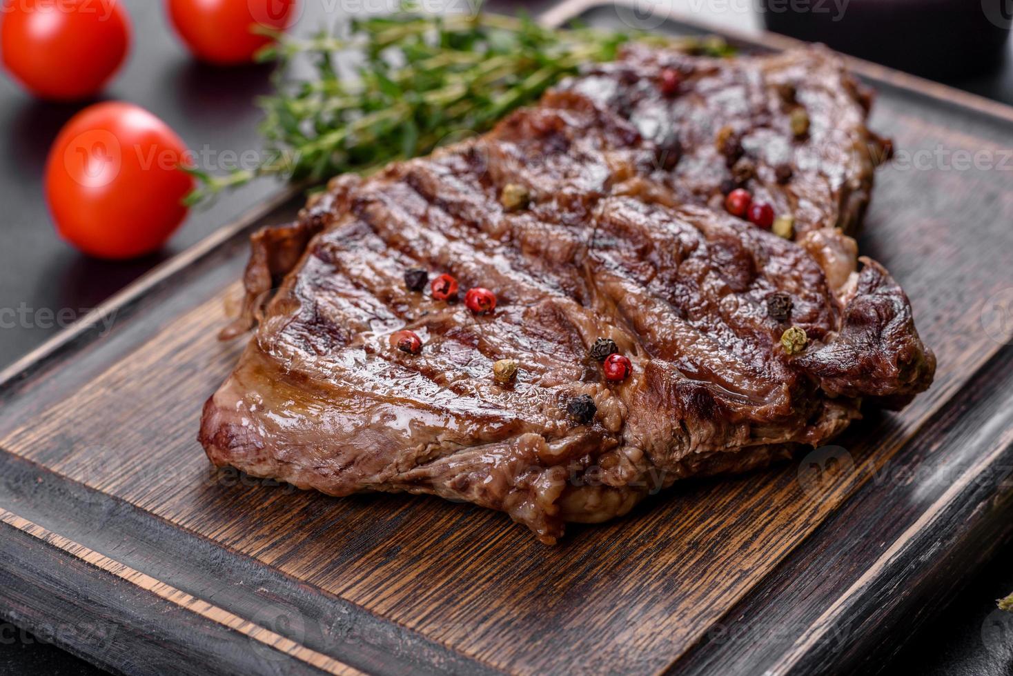 Delicioso bistec de ternera fresca jugosa con especias y hierbas sobre un fondo de hormigón oscuro foto