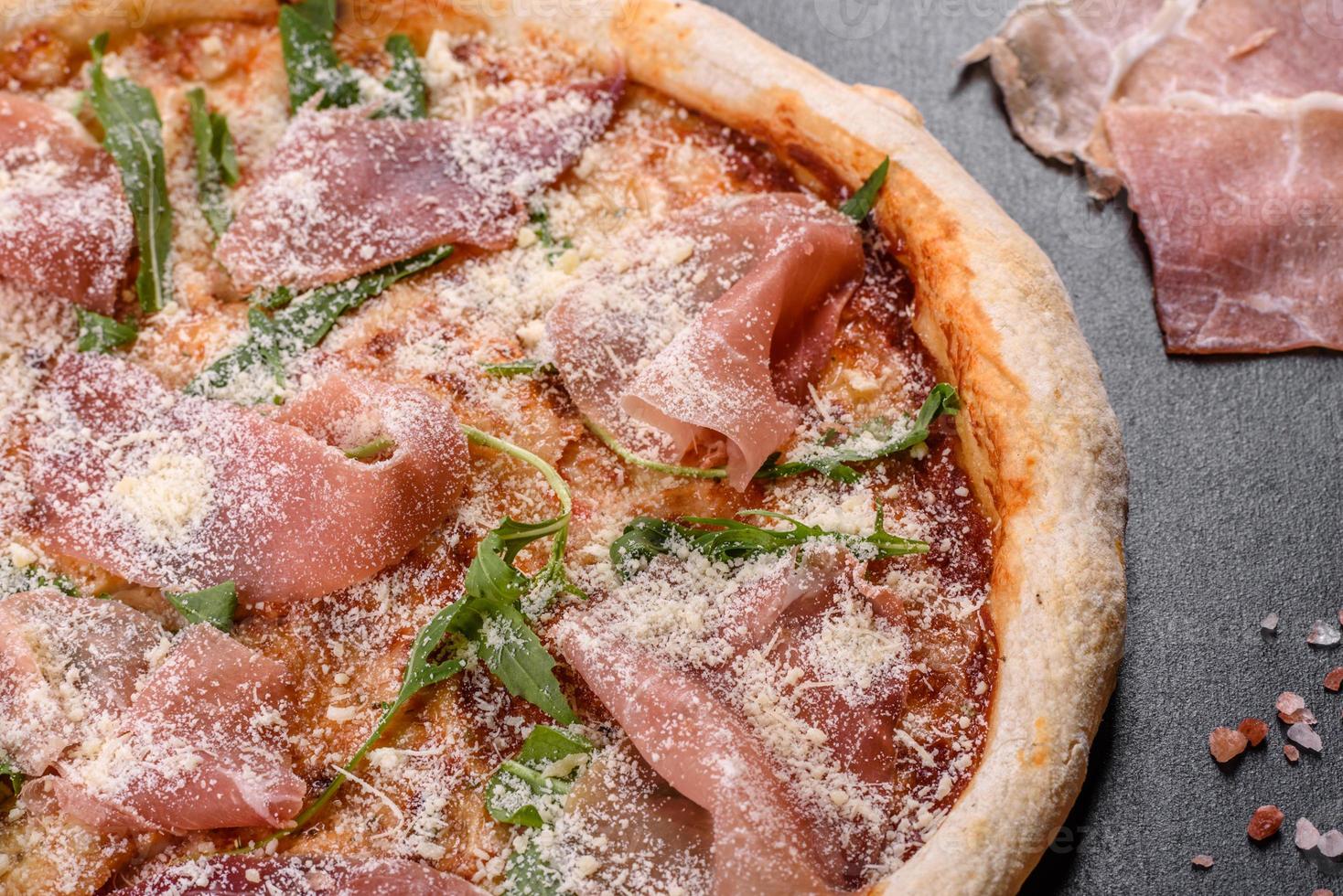 Deliciosa pizza italiana fresca con jamón serrano sobre un fondo de hormigón oscuro foto